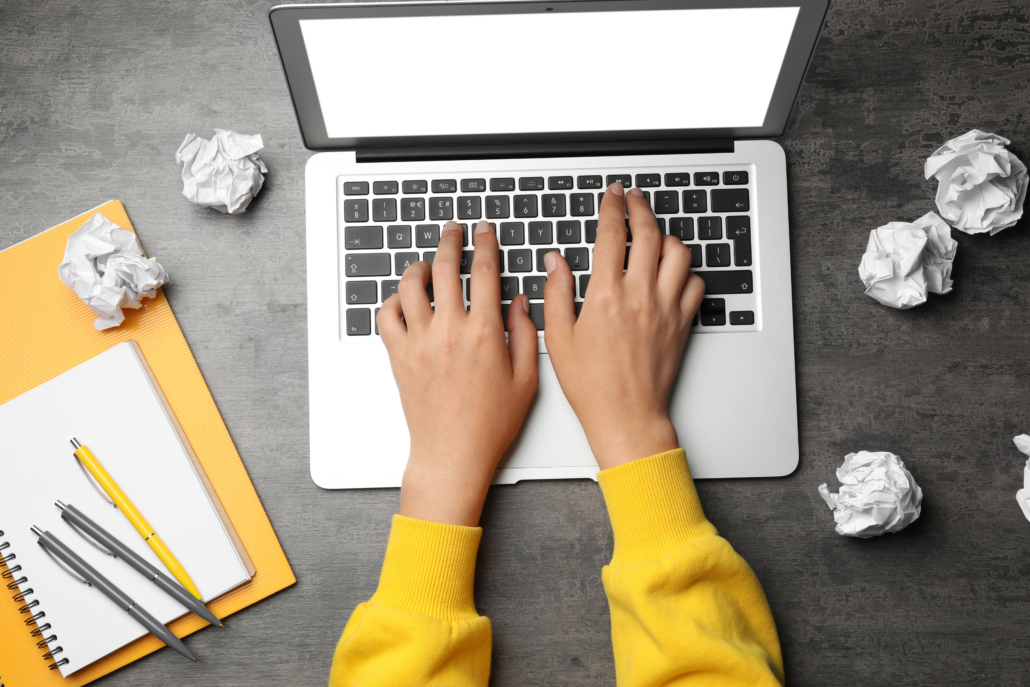 life science marketing agency person working on a laptop with notes and crumpled paper nearby, developing content.